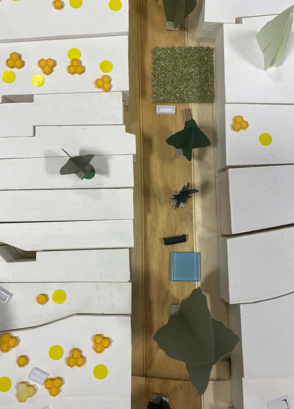 Looking to be the centrepiece of our exhibition, we proposed to create a site model of Dudley Highstreet at 1:200 scale with buildings modelled in a simple form. Local residents and visitors to the exhibition are then invited to decorate a chosen building to how they would envision it sat within the context of a greener Highstreet. We want to tie in our themes of biodiversity and materials by proposing that buildings can, and do, have the potential to be a lot healthier, sustainable, and interactive on the street. This site model also helps gain vital public opinions on the Highstreet and prompts discussion of areas most in need of attention.

To ensure that the model is utilising the MDF to the most efficient standard possible. First, the centres of the massing blocks have been hollowed out. This allows a reduction in materials used as other buildings can be cut in the centres of the model. Then the top is finished with a solid piece.
The waste material is placed into the recycling rack where other students can reuse it; otherwise, if the material left cannot be used for another project, it is recycled correctly by the university.

The model spanned just over 3.4m long and over 50cm wide. With the majority being cut from scrap woods that would fit the jigsaw of the shape, we were able to drastically cut down on waste. We also got some small benches and bee hives printed from recycled plastics, and used dried flowers as trees to represent the green spaces. Ultimately, the model seemed like a huge success, and really helped portray our ideas about Dudley High Street to those who came by. Everyone from Dudley who saw the model knew that it was the High Street, and interacted well with it. The size did make it difficult to move, especially to carry to the site, but it sat nicely in the centre of the the room and really drew people in to interact with it.

The model brought people in from outside to play with, write on, interact with. It became a spectacle for the public to come in and see what was happening and offer their ideas about what could be done.

The event was a success. Many people from the public (those who heard about the event, and those who just happened across it on the day) came in to interact with the model, which sat as the centre piece in the room. Kids liked to play with the pieces while the adults talked about things that could come from actions to help the High Street, not just leave it as is.

SOME OF THE KEY IDEAS WERE:
- The Shops need to be inviting for everyone. It’s no good having these places to go if people would rather take a bus to the next town.
- Just putting up boards across the windows is awful. Paint, Posters, Graffiti: Anything that actually makes the High Street look still alive is better than just wooden boards.
- More Green is needed. While it is obvious that there is a lack of Trees, many people wanted to push for these small bushes or planting spaces that could easily be implemented across the street.
- Spaces for public events or for people to at least gather at. While there is the Market and Fountain, it is not enough for the people of Dudley.
- Something needs to be done about the cars on the High Street. Some were Pro-Removal of all Cars, while some just wanted to limit when they could access the High Street.

Following the exhibition we created a series of drawings with our own interpretation of Sarah Wigglesworth ‘The Dining Table’ drawing. The drawings are a perfect representation of the our interactive model at the ERA Environmental Exhibition and Event. Showing the interaction the public had with the model, as well as the conversations that were held around the model. - Table 2.png